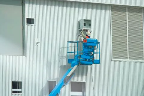 Workers in a baskets are installing sheet, building a factory. Stock Photos