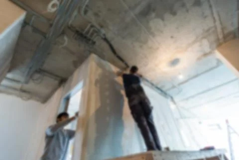 Workers in bokeh. Men are installing the electrical wires on the ceiling in Stock Photos