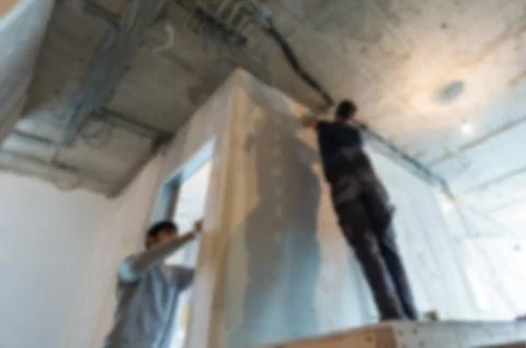 Workers in bokeh. Men are installing the electrical wires on the ceiling in Stock Photos