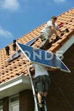 Workers Carrying And Installing Solar Panels On Roof Of New Home, Netherlands