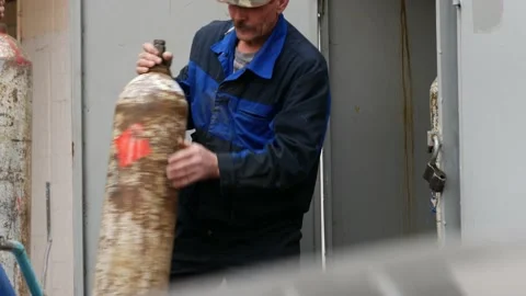 Workers change acetylene gas tank in warehouse. Welder with cigarette in mouth Stock Footage 130971587