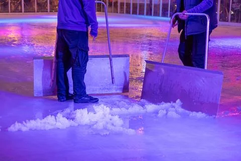 Workers clean an ice skating rink with large metal scrapers under colorful neon Stock Photos