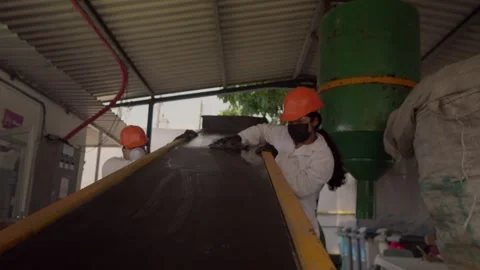Workers clean a plastic crusher conveyor belt at a recycling plant, making Stock Footage 346643665