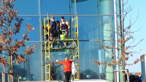 Workers clean a tall building in a city on a sunny day with blue skies Video stock 337531591