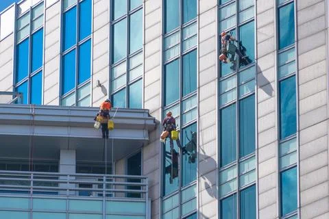 Workers cleaning high-rise windows with safety gear Stock Photos