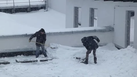 Workers clear snow from a rooftop during a winter storm in a city Stock Footage 330156451