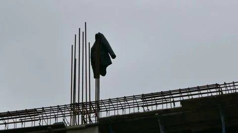 Worker’s coat blowing in wind on rebar at unfinished building site Stock Footage 317827253