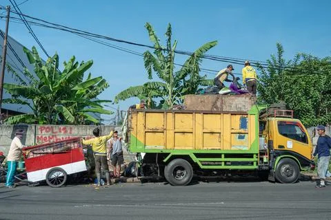 Workers collect and load garbage into a yellow truck on a busy street Stock Photos