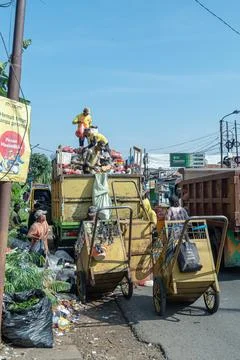Workers collect and load garbage into a yellow truck on a busy street Stock Photos