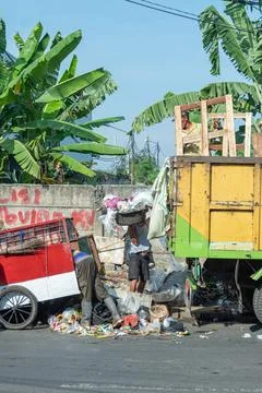 Workers collect and load garbage into a yellow truck on a busy street Stock Photos