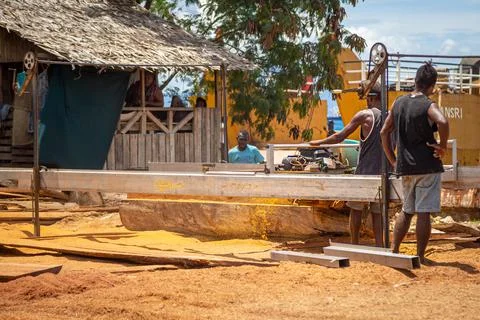 Workers cutting raw logs into lumber on the street-side of an industrial area Stock Photos