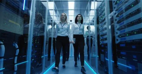 Workers in a data center walking between rows of server racks Stock Photos