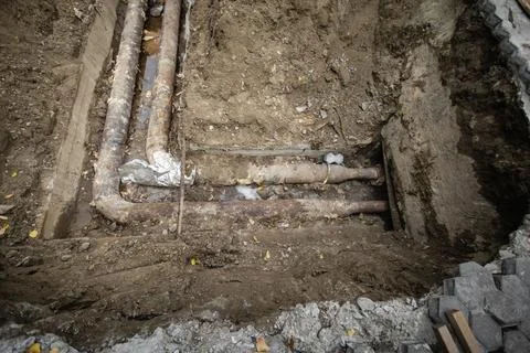 Workers dig deep to uncover old pipes buried beneath the ground in an urban a Photos