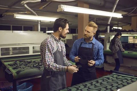 Workers discussing production process standing at cutting machine in shoe making Stock Photos