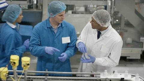 Workers discussing while inspecting cosmetic bottles on production line Stock Footage 107967872