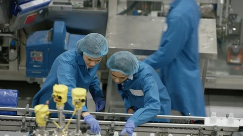 Workers discussing while inspecting cosmetic bottles on production line Stock Footage 107968664