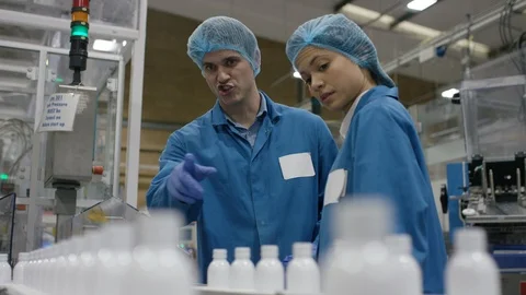 Workers discussing while inspecting cosmetic bottles on conveyor belt Stock Footage 107976296