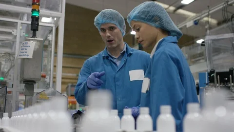 Workers discussing while inspecting cosmetic bottles on conveyor belt Video stock 107976444