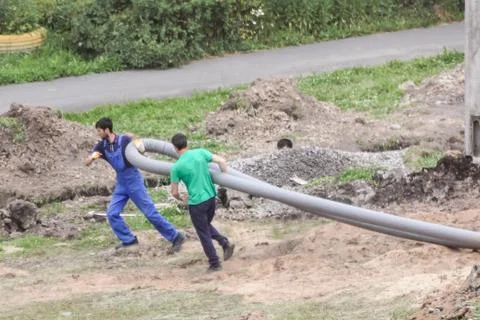 Workers drag pipe to the trench. Stock Photos