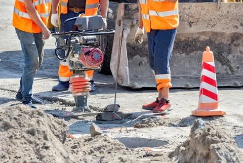 Workers engage in construction activity using a compactor in a busy worksite Stock Photos