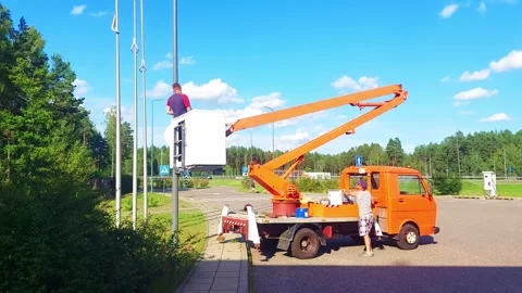Workers fix equipment high above ground near a parking lot on a sunny day in the Stock Footage 325312970