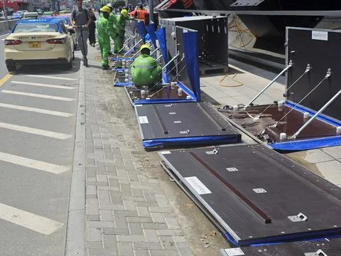 Workers in green uniforms install modular flood barriers on a city sidewalk n Stock Photos