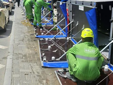 Workers in green uniforms install modular flood barriers on a city sidewalk Stock Photos