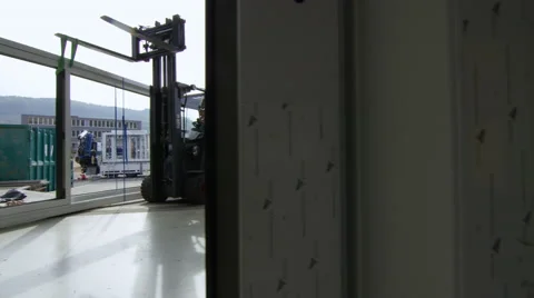 Workers guide a large window frame out of a factory with a forklift truck. Stock Footage 63012225