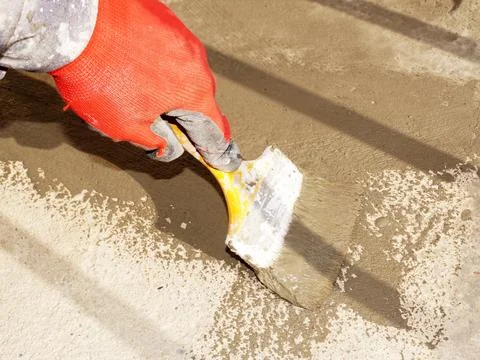A worker's hand applies a waterproofing solution to a concrete floor with a b Stock Photos