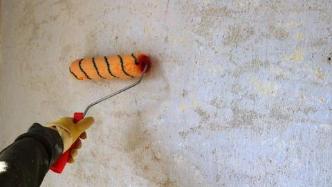Worker's hand with a bright roller on the background of a light repaired wall Stock Photos