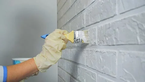Worker's hand in gloves paints a wall of white paint with a wooden brush. Stock Footage 144276855