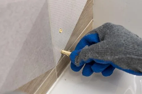 Worker's hand inserts a plastic dowel pin into a drilled hole 库存照片