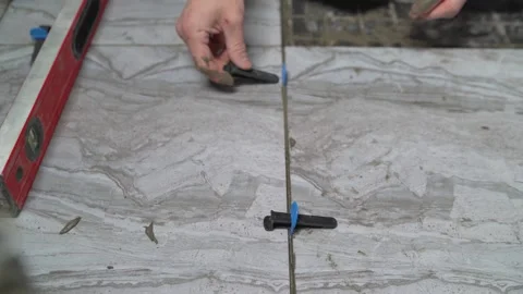 Worker's hand installing gray floor tiles using a leveling system. Stock Footage 331503784