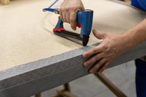 Worker's hand operates a blue pneumatic stapler. Stock Photos