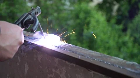 Worker's hand welding a metal structure outdoors using manual metal arc welding Stock Footage 334812784