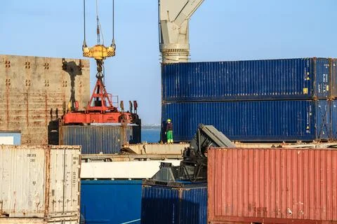 Workers handle crane loading cargo containers at a shipping terminal Stock Photos