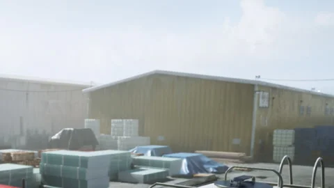 Workers handle materials in a construction area near a storage building Vidéo 343576802
