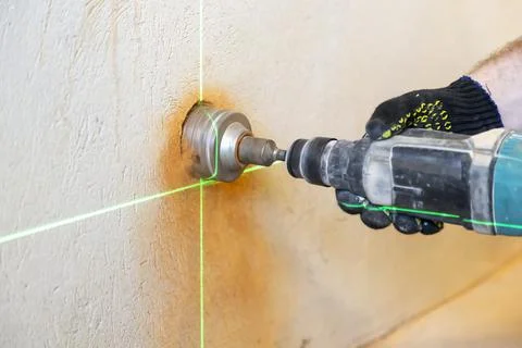 Worker's hands drill a hole in the wall to install an electrical outlet, close 库存照片
