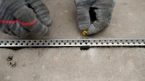 Worker's hands in gloves assembling a metal profile on a concrete floor. Stock-Fotos