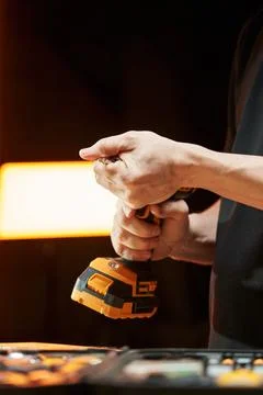 Worker's hands install a cross bit in an electric screwdriver with a replaceable Stock Photos