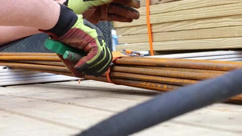 Workers hands remove tie down ratchet strap from a bundle of rusty rebar. Stock Footage 156670650