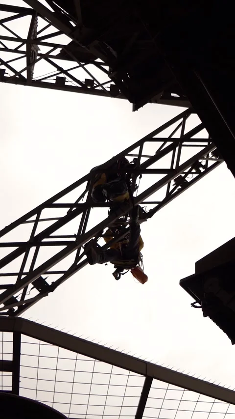 Workers in Harnesses Climbing Steel Structure Silhouetted Against Sky Stock Footage 334939589