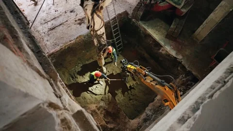 Workers in helmets dump the earth with shovels onto the bucket of the tractor Stock Footage 263773169