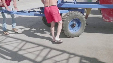 Workers help move the blue trailer with the yacht over the concrete surface Stock Footage 77292933