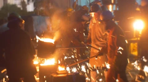 Workers Holding Burning Liquid Metal in Ladle Silhouettes at Night Festival of Stock Footage 64358452
