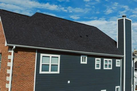 Workers install new roofing on a two-story house made of brick and siding. Cl Stock Photos