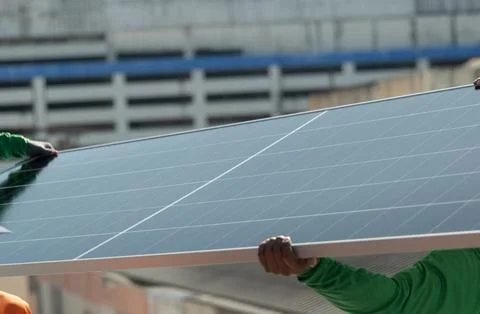 Workers install solar panels on a rooftop during a sunny day in an urban area Foto stock