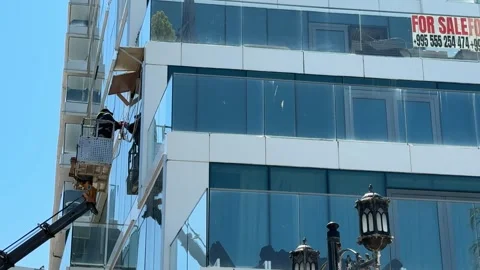 Workers installing glass facade on modern office building under clear sky Stock Footage 336399075
