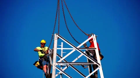Workers Installing Steel Tower Structure at Height Against Blue Sky Stock Footage 332611726