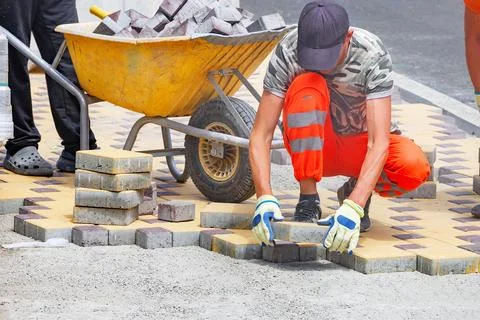 Workers lay down bricks for pavement on a city street during daylight hours.. Stock Photos